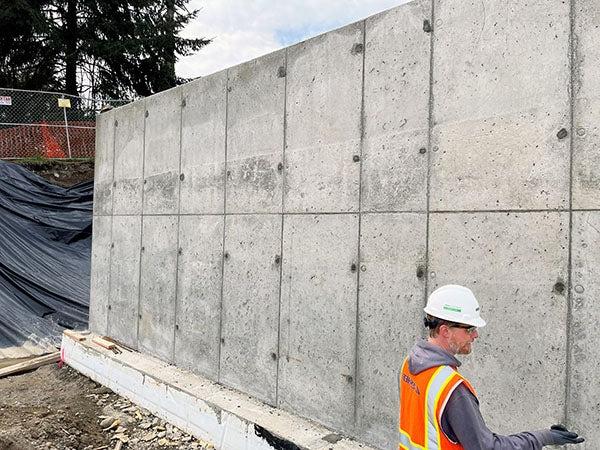 a very tall concrete wall with a person standing in front of it. the person comes up about 1/3 of the height