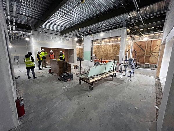 interior of a large room under construction with workers and equipment, a metal ceilding, and partially finished walls