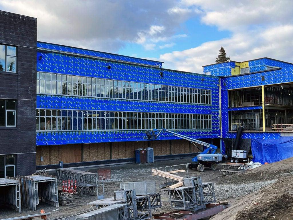 a section of a 3-story building with blue weatherproofing and glass windows