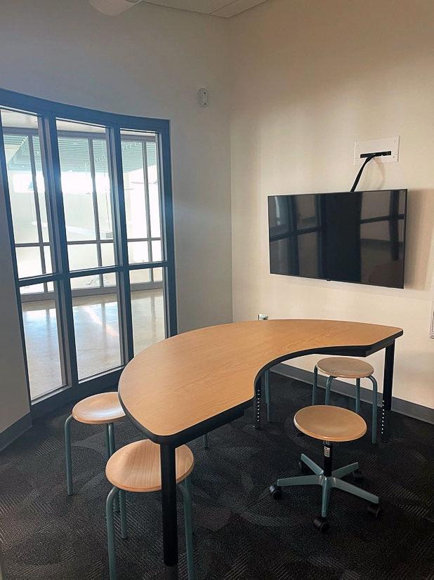 a small room with a video screen, windows on one wall, a half circle table and five stools