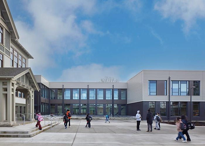 a 2 story building adjoins a historic building in an L shape with a plaza in front of both. students walk in the plaza